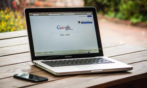 Laptop with Google search page on wooden table outdoors.